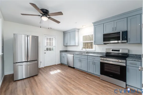 a kitchen with granite countertop a refrigerator a stove top oven a sink dishwasher and wooden floor