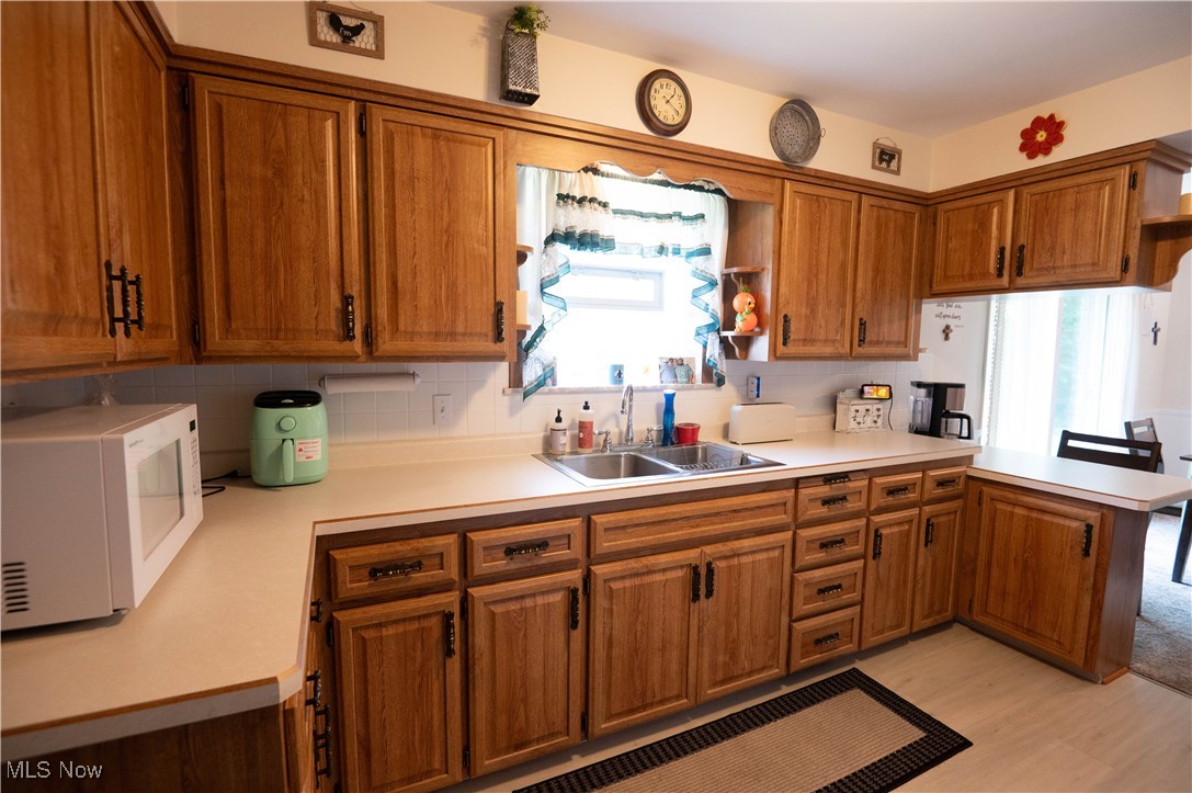 1074 South Meridian Road Youngstown, OH 44515 - Photo 17 of 42 Kitchen featuring white microwave, brown cabinetry, a peninsula, and light countertops