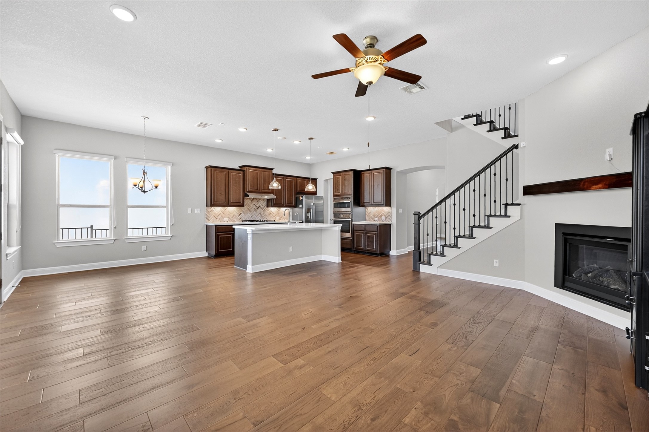 1201 Positano Pass Leander, TX 78641 - Photo 20 of 40 Open-concept living space featuring wood-finish flooring, a kitchen island, recessed lighting, a ceiling fan, and a built-in fireplace with a wooden mantel
