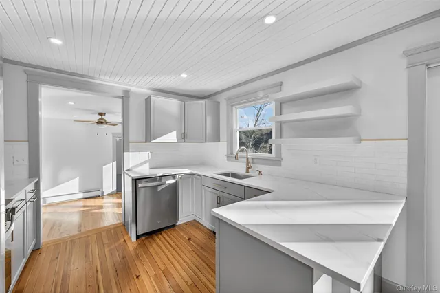 a kitchen with a sink dishwasher a stove and white cabinets with wooden floor