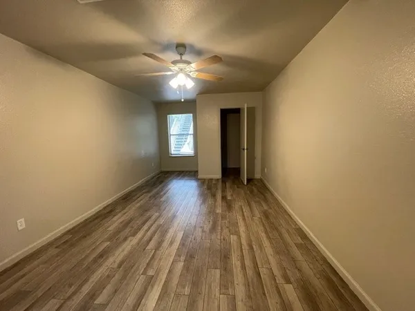 a view of empty room with wooden floor and fan