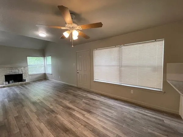 an empty room with wooden floor fan and windows