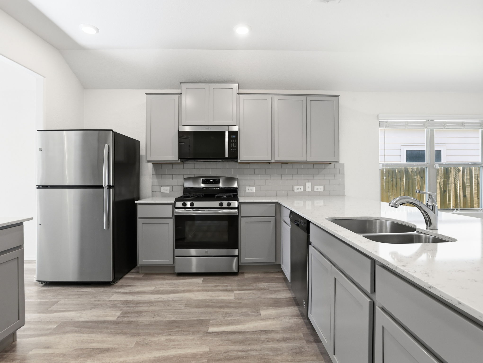 5900 Bell Tower Lane Austin, TX 78747 - Photo 2 of 26 Kitchen featuring gray cabinets, stainless steel appliances, light stone counters, light wood finished floors, and decorative backsplash