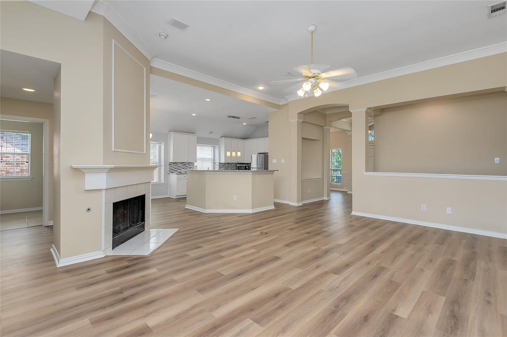1404 Ranch Hill Drive Irving, TX 75063 - Photo 11 of 31 Expansive living area featuring wood-finish flooring, a white mantel fireplace with a tile hearth, crown molding, and a ceiling fan with integrated lighting