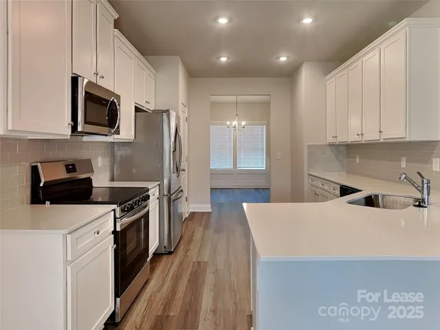 a kitchen with stainless steel appliances a stove top oven a sink a refrigerator white cabinets and wooden floor