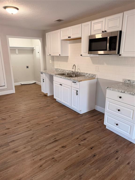Kitchen featuring stainless steel microwave, white cabinets, light countertops, a textured ceiling, and dark wood-type flooring