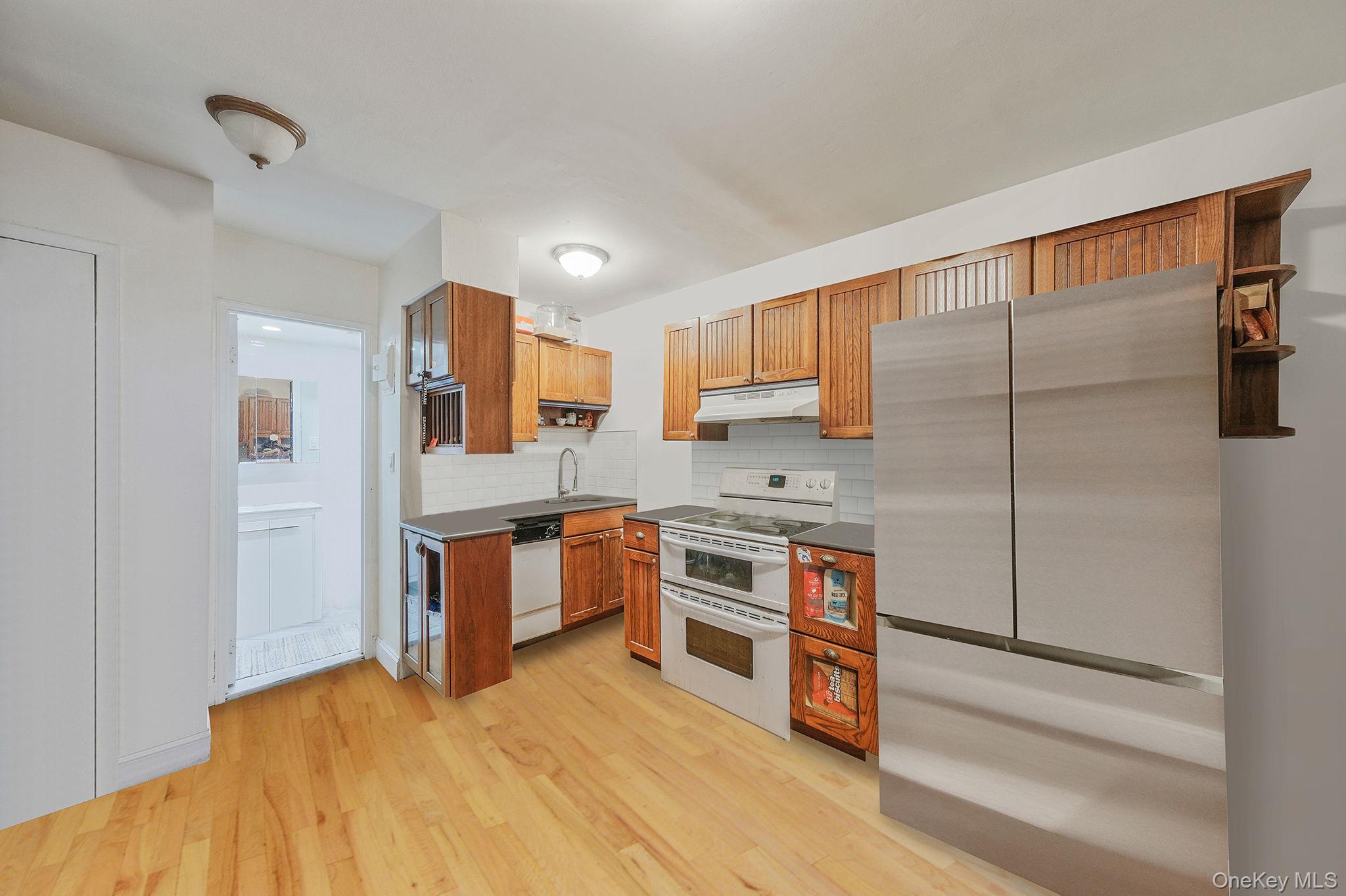 403 East 87th Street, Unit 3B Manhattan, NY 10128 - Photo 5 of 25 Kitchen with dark countertops, white appliances, brown cabinetry, tasteful backsplash, and light wood-style flooring
