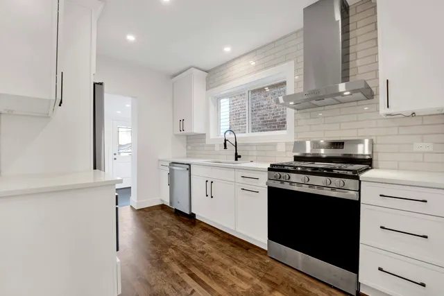 a kitchen with stainless steel appliances granite countertop a stove a sink and white cabinets