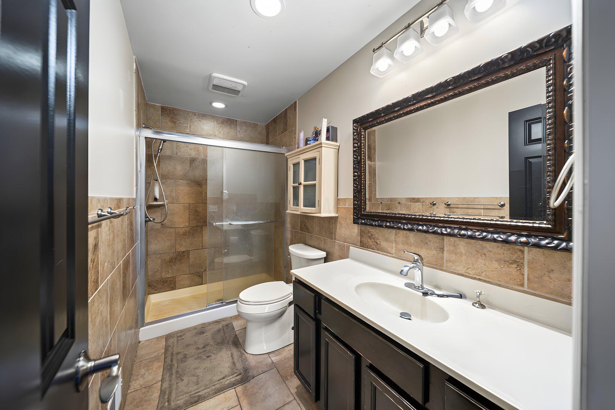 6344 Post Road Dublin, OH 43017 - Photo 19 of 45 Tiled shower with sliding glass door, vanity with integrated sink and chrome faucet, framed mirror, and built-in storage cabinet