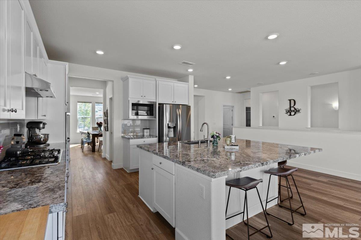 10385 Alchemy Court Reno, NV 89521 - Photo 8 of 40 a kitchen with stainless steel appliances granite countertop a stove refrigerator a dining table and chairs with wooden floor