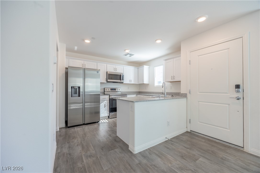 12185 Scarlet Ember Road, Unit 4 Las Vegas, NV 89183 - Photo 4 of 40 Kitchen featuring stainless steel appliances, white cabinetry, light stone countertops, light wood-style floors, and recessed lighting