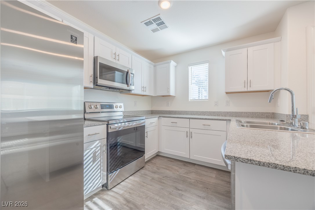 12185 Scarlet Ember Road, Unit 4 Las Vegas, NV 89183 - Photo 5 of 40 Kitchen with appliances with stainless steel finishes, white cabinetry, light wood-style floors, and light stone countertops