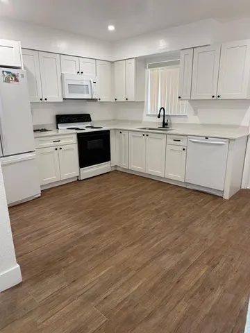 a kitchen with stainless steel appliances granite countertop a sink a stove a refrigerator with white cabinets and wooden floor