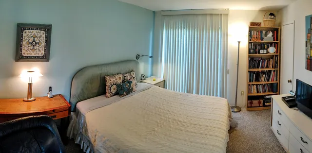 a bedroom with a bed a book shelf and a lamp on dresser