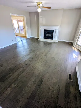 an empty room with wooden floor fireplace and windows