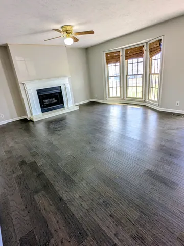 an empty room with wooden floor fireplace and windows
