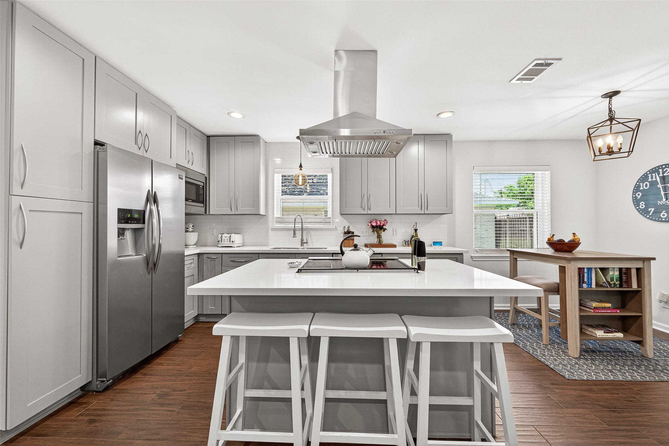 2610 Teague Road Houston, TX 77080 - Photo 4 of 49 This modern kitchen features sleek gray cabinets, stainless steel appliances, and a central island with bar seating. It has ample natural light, wood-like tile flooring, and a cozy dining nook, creating a stylish and functional space.