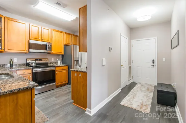 a kitchen with stainless steel appliances kitchen island granite countertop wooden cabinets a refrigerator a stove a sink and dishwasher with wooden floor