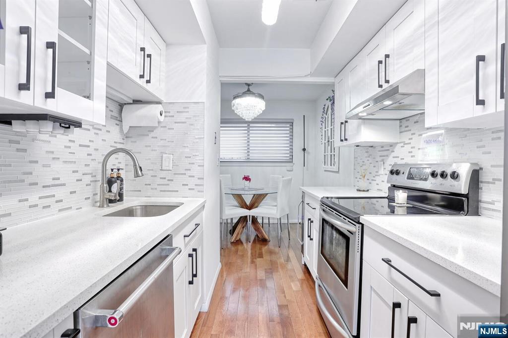 1110 River Road, Unit 105 Edgewater, NJ 07020 - Photo 8 of 19 a kitchen with stainless steel appliances a sink dishwasher stove and white cabinets with wooden floor