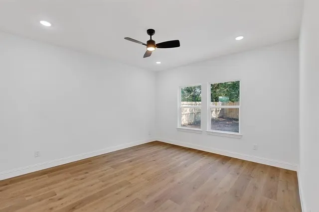 an empty room with wooden floor fan and windows