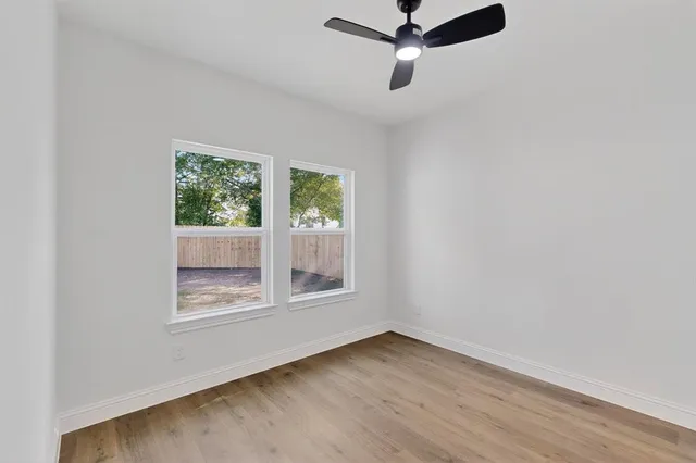 an empty room with wooden floor ceiling fan and windows