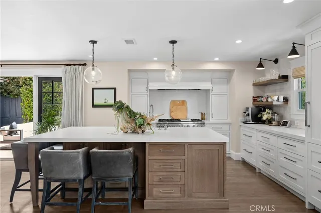 a kitchen with kitchen island granite countertop a stove a sink a dining table and chairs with wooden floor