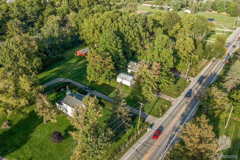 59380 10 Mile Road South Lyon, MI 48178 - Photo 7 of 53 Aerial perspective showcasing the property with expansive green space, mature trees, a paved driveway, and a roadside location