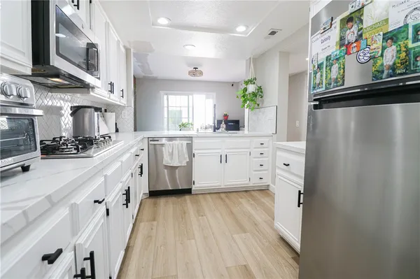 a large white kitchen with stainless steel appliances a lot of counter space and wooden floor