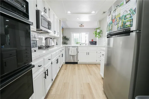 a large white kitchen with stainless steel appliances granite countertop a refrigerator a sink dishwasher a stove and white cabinets with wooden floor
