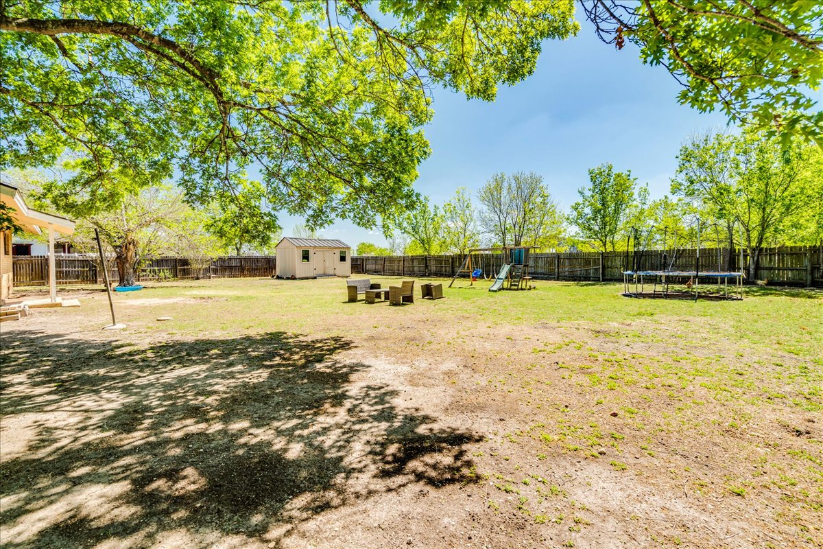 500 Blackjack Street Lockhart, TX 78644 - Photo 25 of 27 Fenced backyard featuring a trampoline, a playground, and a storage unit