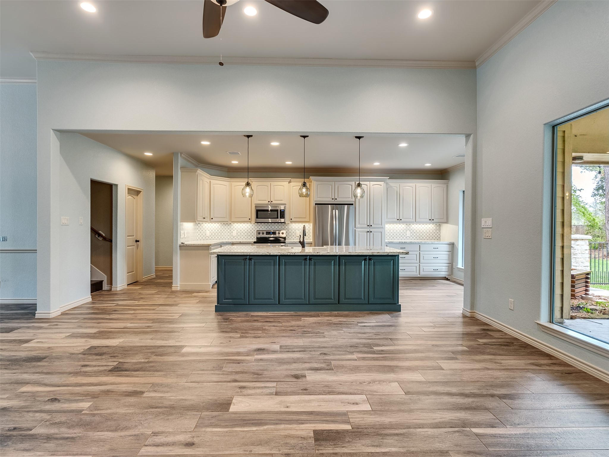 18005 Cindy Lane Conroe, TX 77302 - Photo 11 of 49 This photo showcases a spacious, open-concept kitchen. The kitchen features a large island with custom cabinetry, modern pendant lighting, stainless steel appliances. Natural light fills the space through a large window, enhancing its bright and airy feel.