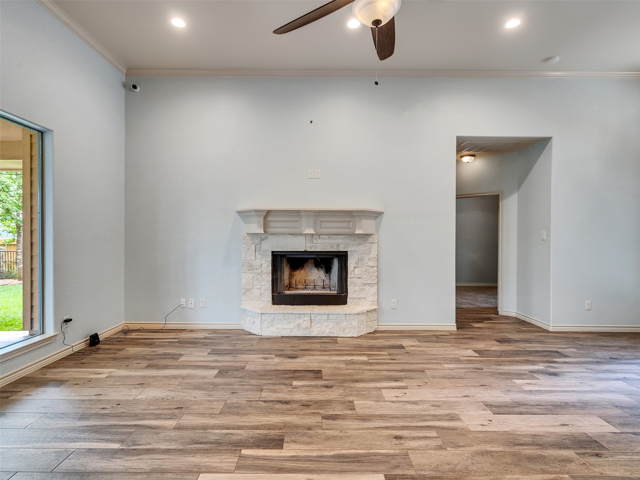 18005 Cindy Lane Conroe, TX 77302 - Photo 22 of 49 This spacious living room features a modern, light color scheme with wood-look flooring and a stone fireplace as a focal point. It has recessed lighting and a ceiling fan, with large windows offering natural light and views of the backyard.