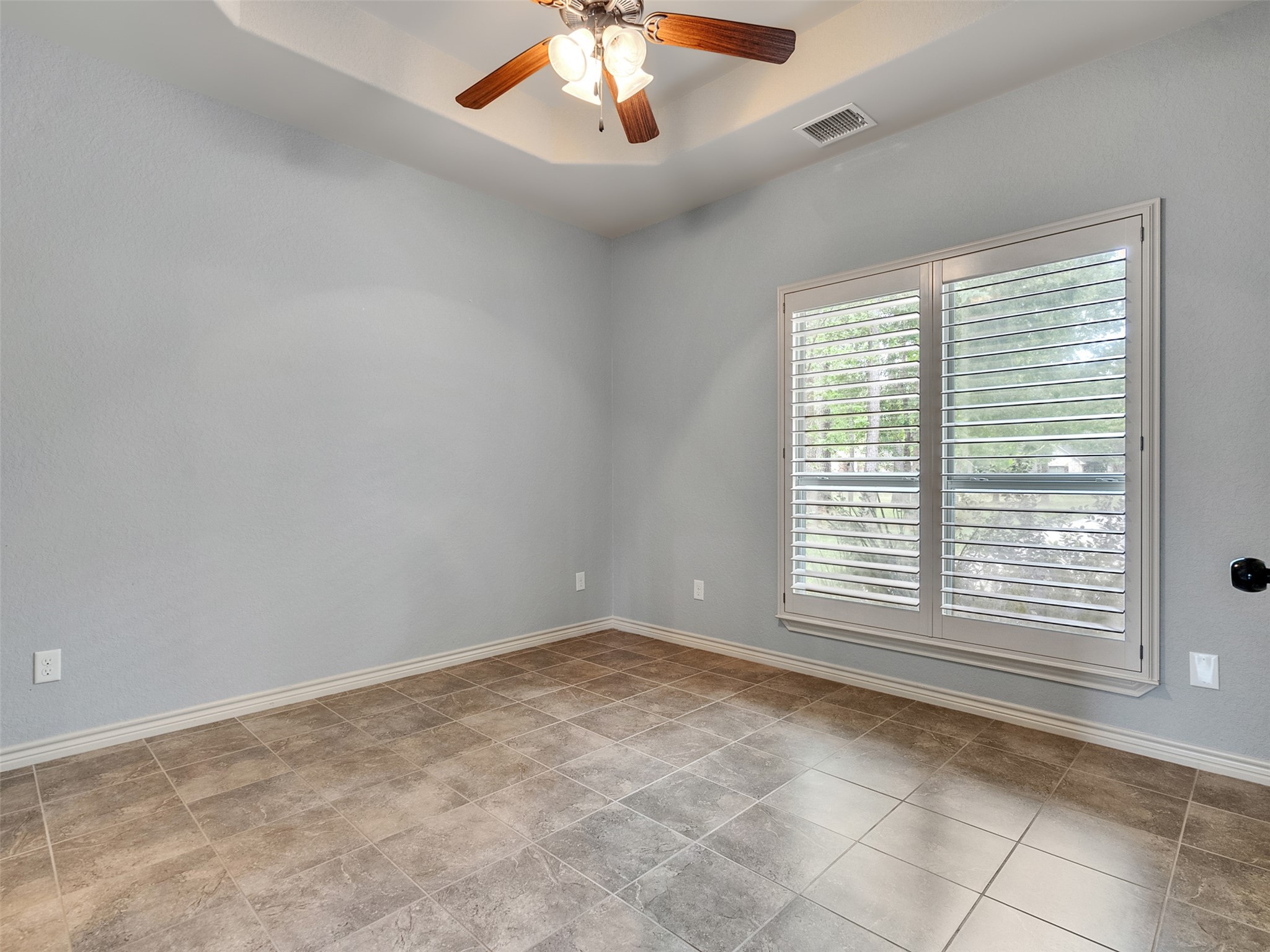 18005 Cindy Lane Conroe, TX 77302 - Photo 23 of 49 Bedroom neutral is neutral walls and tiled flooring, with a ceiling fan overhead. A large window with shutters allows natural light to filter in, creating a bright and airy space.