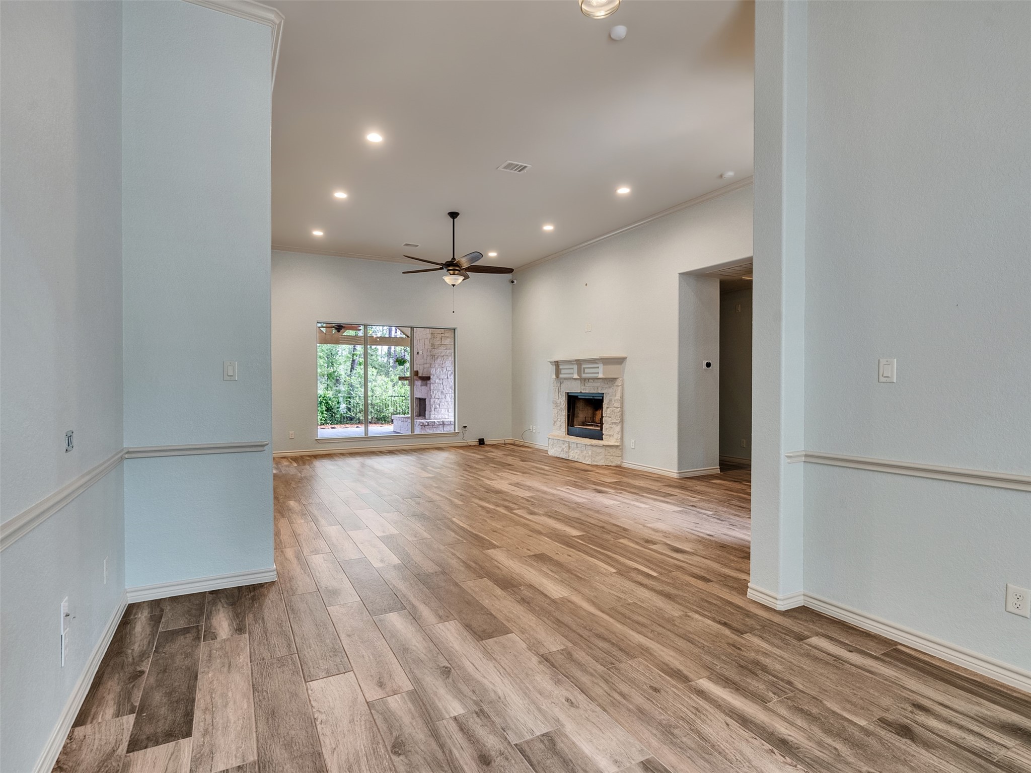 18005 Cindy Lane Conroe, TX 77302 - Photo 9 of 49 Spacious living room with wood-look flooring, a cozy fireplace, and recessed lighting. The room features a ceiling fan and large windows, offering a view of lush greenery outside.