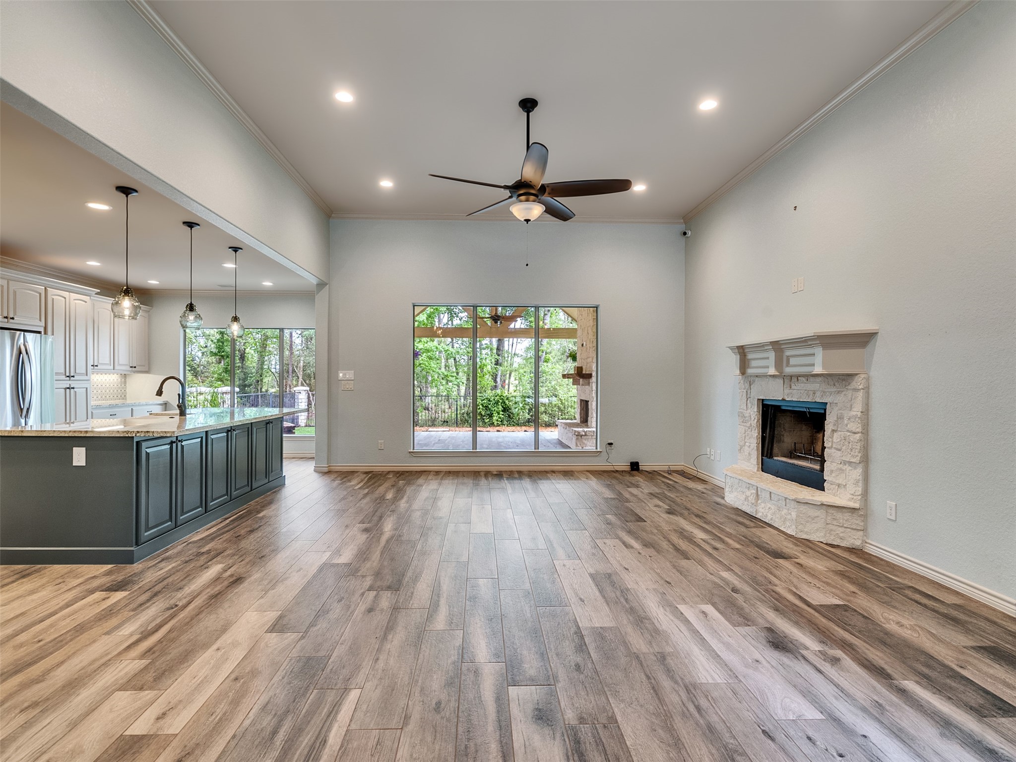 18005 Cindy Lane Conroe, TX 77302 - Photo 10 of 49 This spacious open-concept living area features a modern kitchen with an island, pendant lighting, and stainless steel appliances. The room includes tile wood like-style flooring, a cozy stone fireplace, and large windows offering views of a lush backyard, creating a perfect blend of comfort and style.