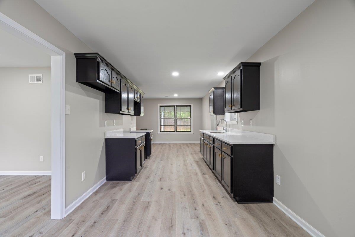 6410 Coteswood Road Memphis, TN 38134 - Photo 6 of 25 Kitchen with a sink, light wood finished floors, dark cabinetry, light countertops, and baseboards