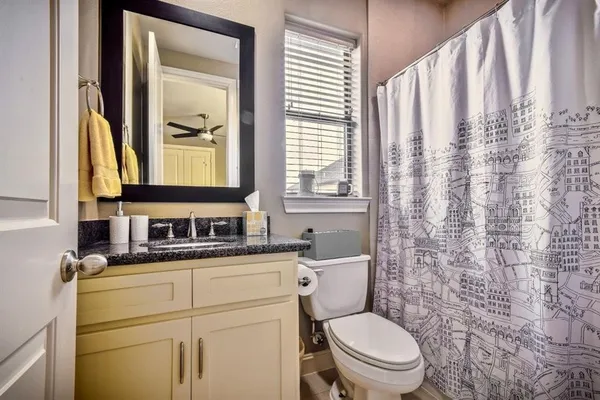 a bathroom with a granite countertop toilet sink and mirror with window