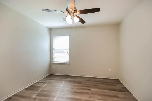 an empty room with wooden floor fan and windows