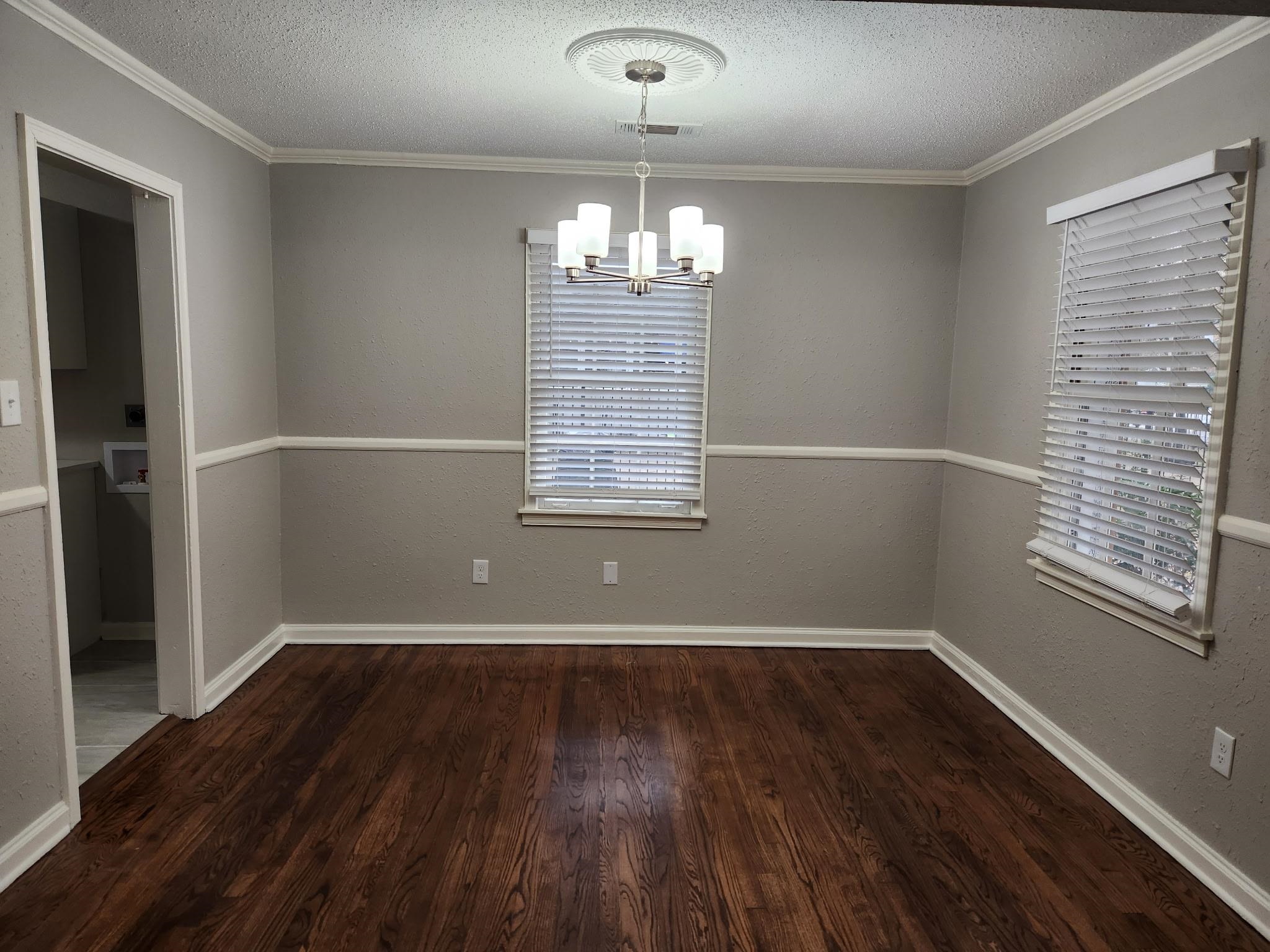 866 Colonial Road Memphis, TN 38117 - Photo 7 of 15 Unfurnished dining area featuring a textured ceiling, a chandelier, ornamental molding, dark wood-style flooring, and a textured wall
