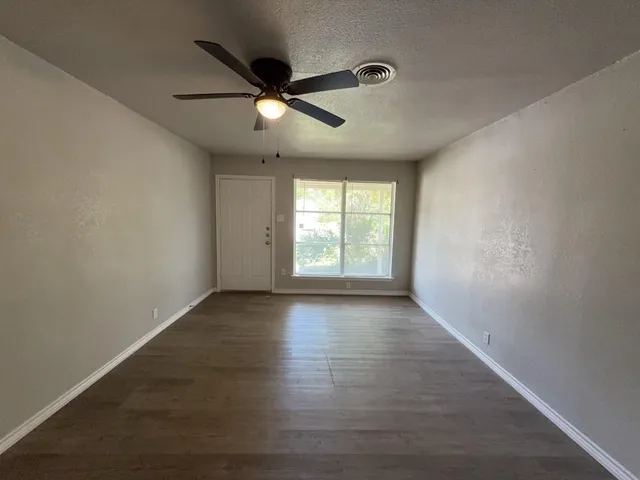 an empty room with wooden floor fan and windows