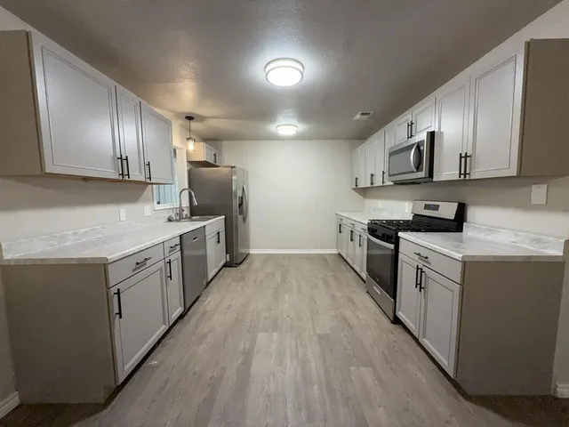 a kitchen with stainless steel appliances a sink dishwasher a stove top oven a refrigerator with grey cabinets and wooden floor