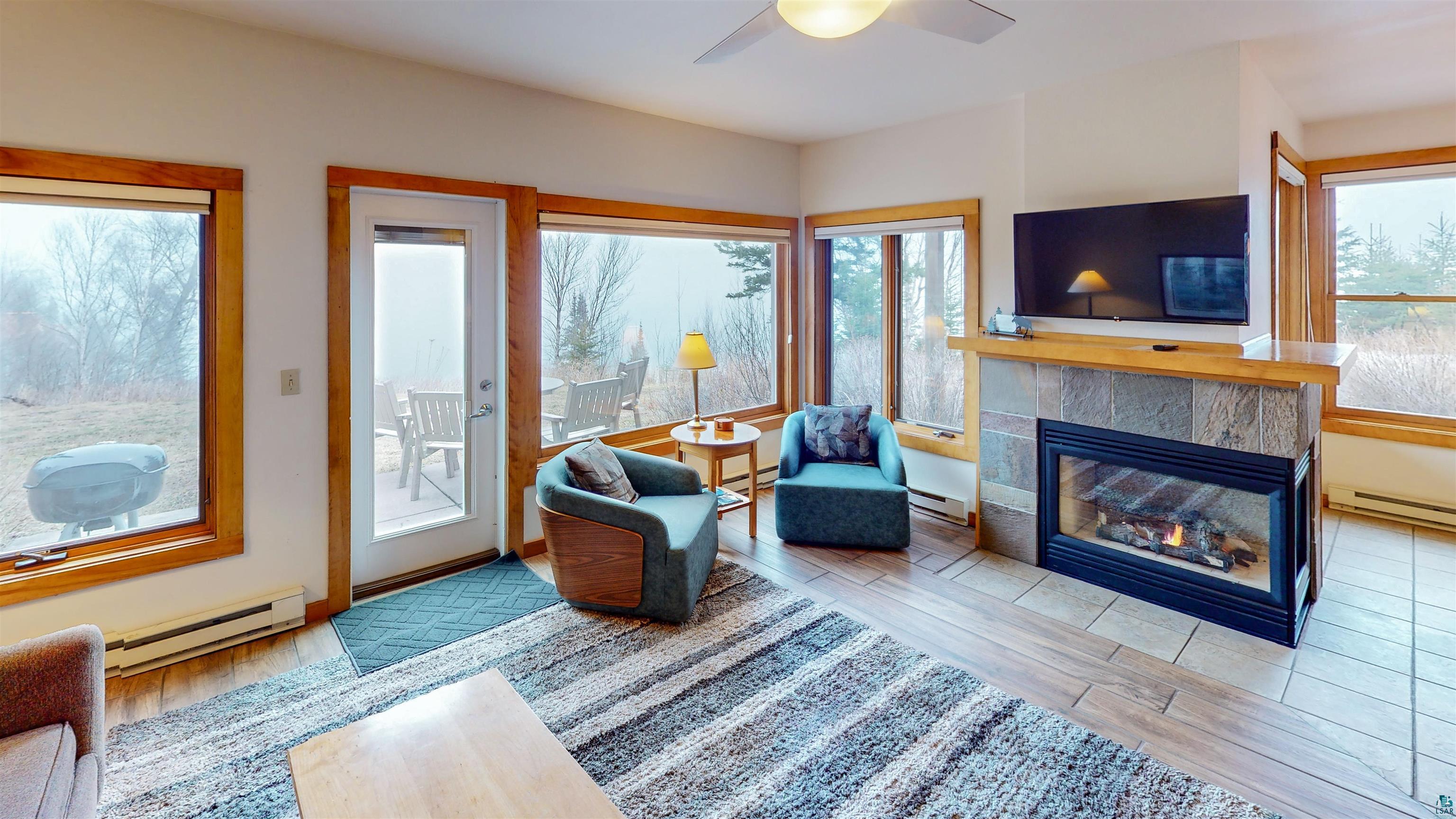 504-506 Poplar River Road, Unit 505 Lutsen, MN 55612 - Photo 29 of 39 Living area featuring a stone-clad fireplace with hearth, multiple large windows, a glass-paned door opening to an outdoor patio, and tile flooring