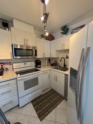 a kitchen with stainless steel appliances a stove a microwave a sink a refrigerator white cabinets and wooden floor