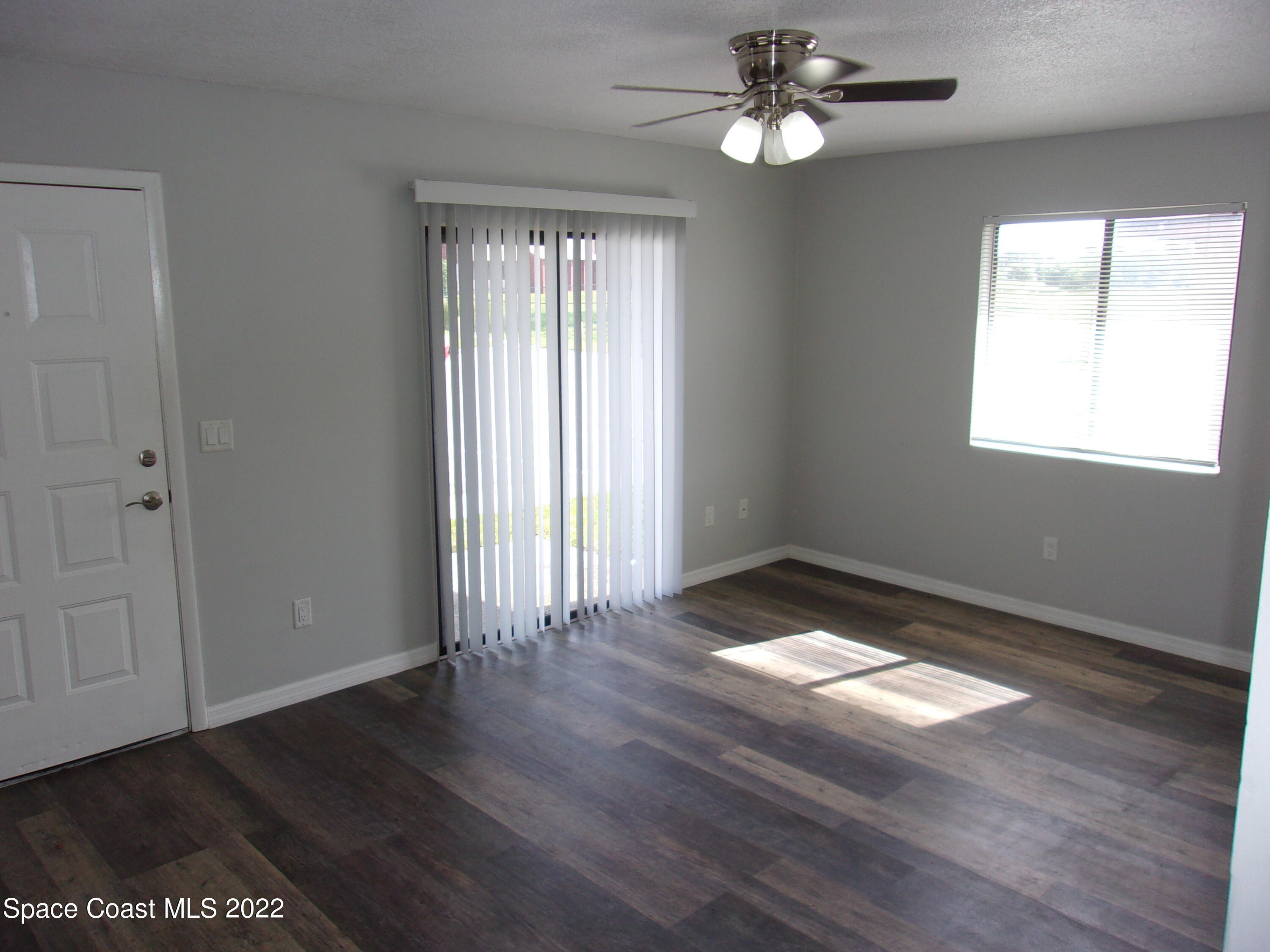 1050 North Fiske Boulevard, Unit 406 Cocoa, FL 32922 - Photo 4 of 11 an empty room with wooden floor chandelier fan and windows