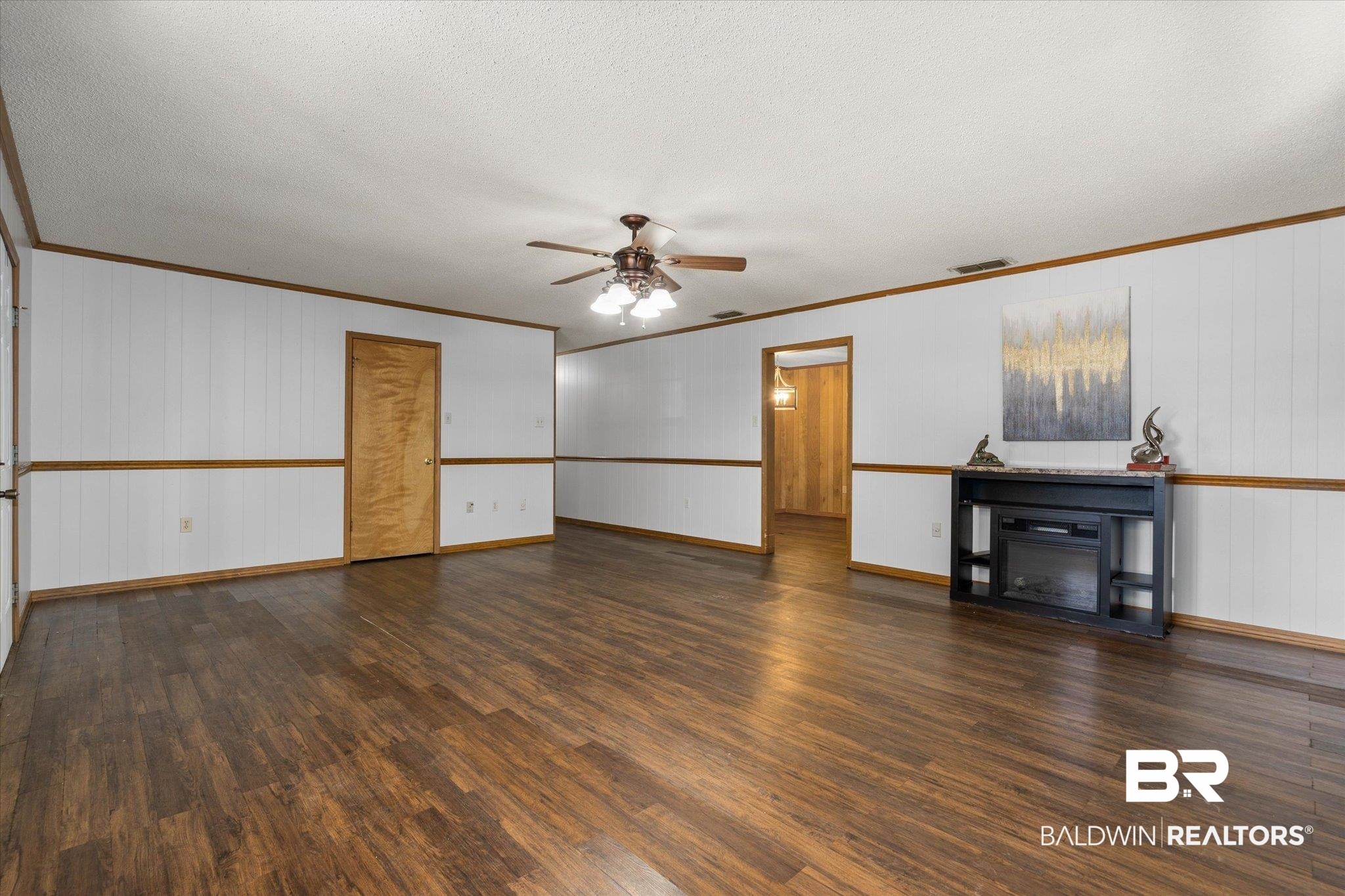5503 Darring Street Satsuma, AL 36572 - Photo 6 of 31 Unfurnished living room with crown molding, wood finished floors, a ceiling fan, wooden walls, and a glass covered fireplace