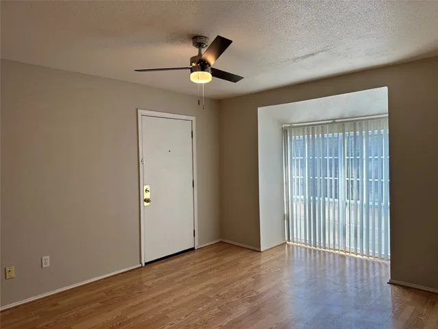 an empty room with wooden floor chandelier fan and windows