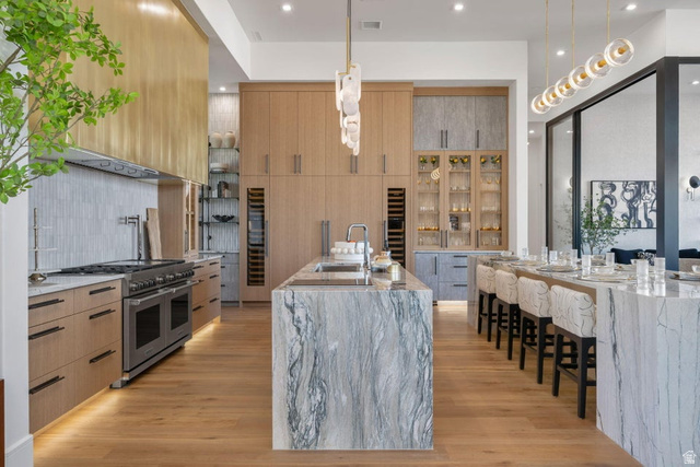 2867 East Granite Way St. George, UT 84790 - Photo 5 of 69 Gourmet kitchen featuring a large waterfall island with integrated sink, a second waterfall island with seating, a professional-grade range, full-height custom cabinetry, and wood-finish flooring