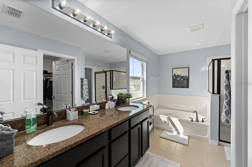 754 Andalusia Loop Davenport, FL 33837 - Photo 11 of 28 a bathroom with a granite countertop double vanity sink a mirror and a bathtub