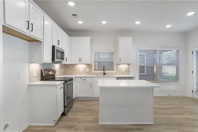 a kitchen with stainless steel appliances granite countertop a sink a stove a refrigerator cabinets and a window