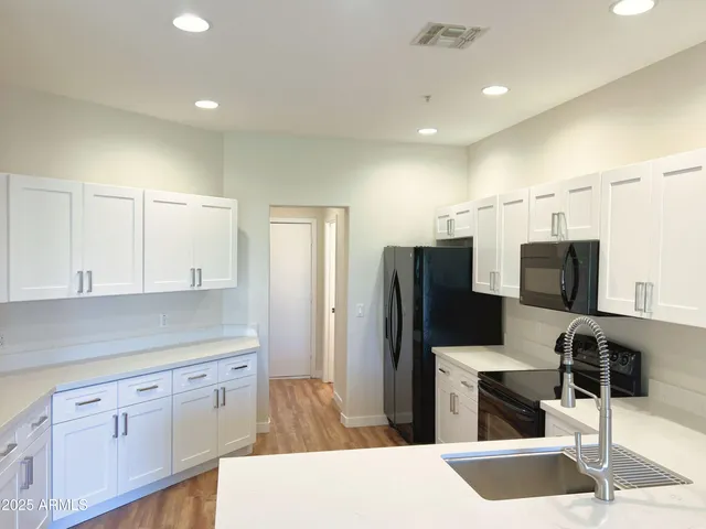 a kitchen with stainless steel appliances kitchen island granite countertop a refrigerator a stove a sink and white cabinets with wooden floor